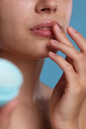 Photo of Young woman with lip balm on light blue background, closeup