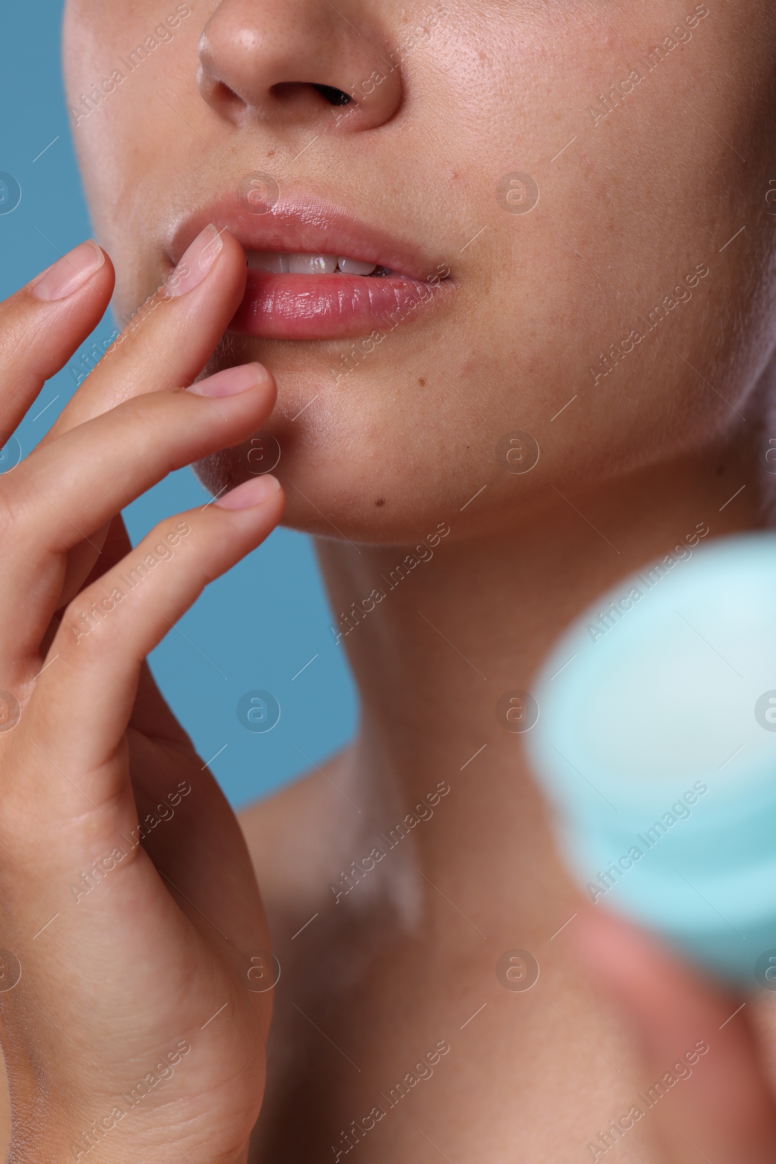 Young woman with lip balm on light blue background, closeup Photo of Young woman with lip balm on light blue background, closeup