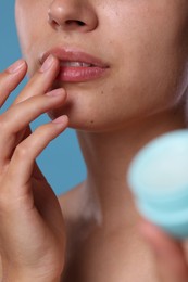 Photo of Young woman with lip balm on light blue background, closeup