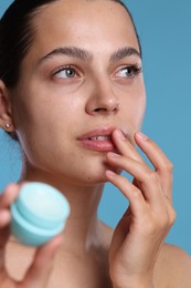 Photo of Young woman with lip balm on light blue background
