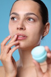Photo of Young woman with lip balm on light blue background