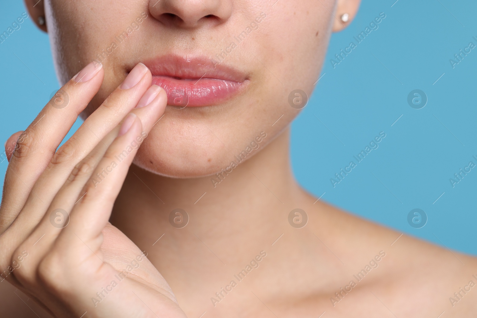 Young woman with lip balm on her lips against light blue background, closeup Photo of Young woman with lip balm on her lips against light blue background, closeup