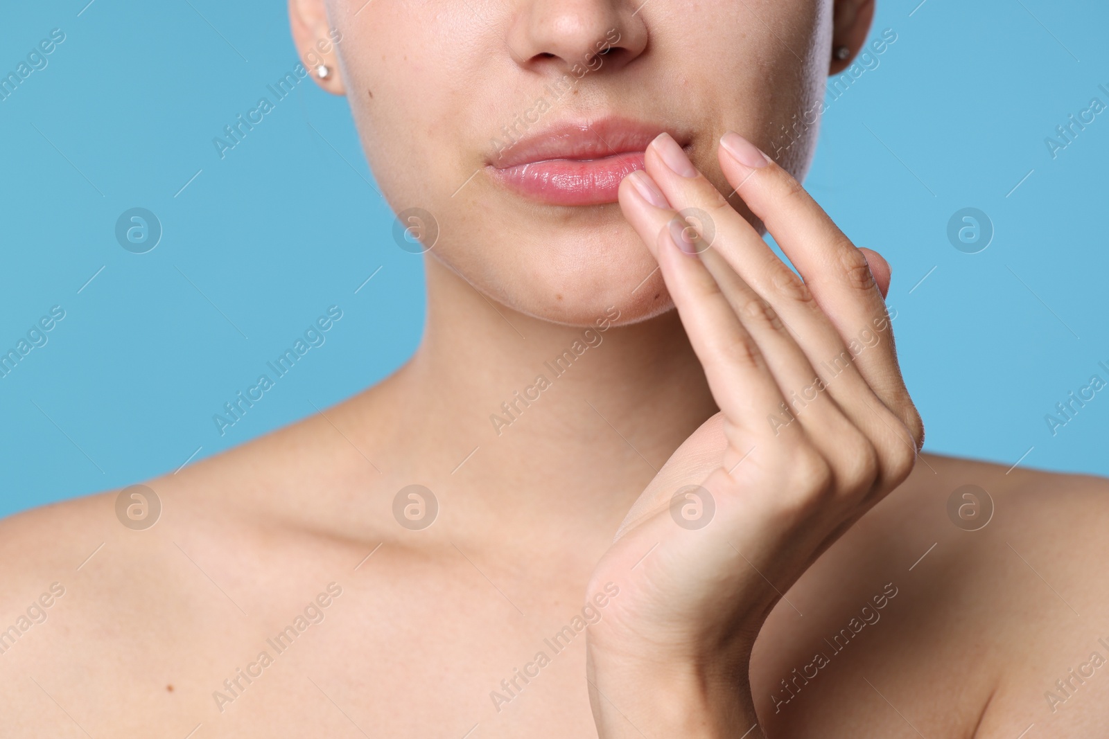 Young woman with lip balm on her lips against light blue background, closeup Photo of Young woman with lip balm on her lips against light blue background, closeup