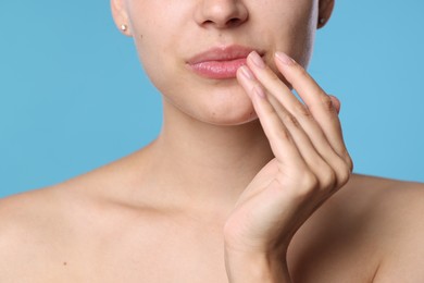 Photo of Young woman with lip balm on her lips against light blue background, closeup