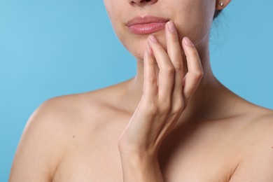 Photo of Young woman with lip balm on her lips against light blue background, closeup