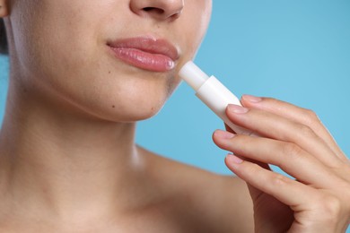 Photo of Young woman with lip balm on light blue background, closeup