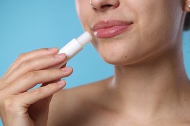 Photo of Young woman with lip balm on light blue background, closeup