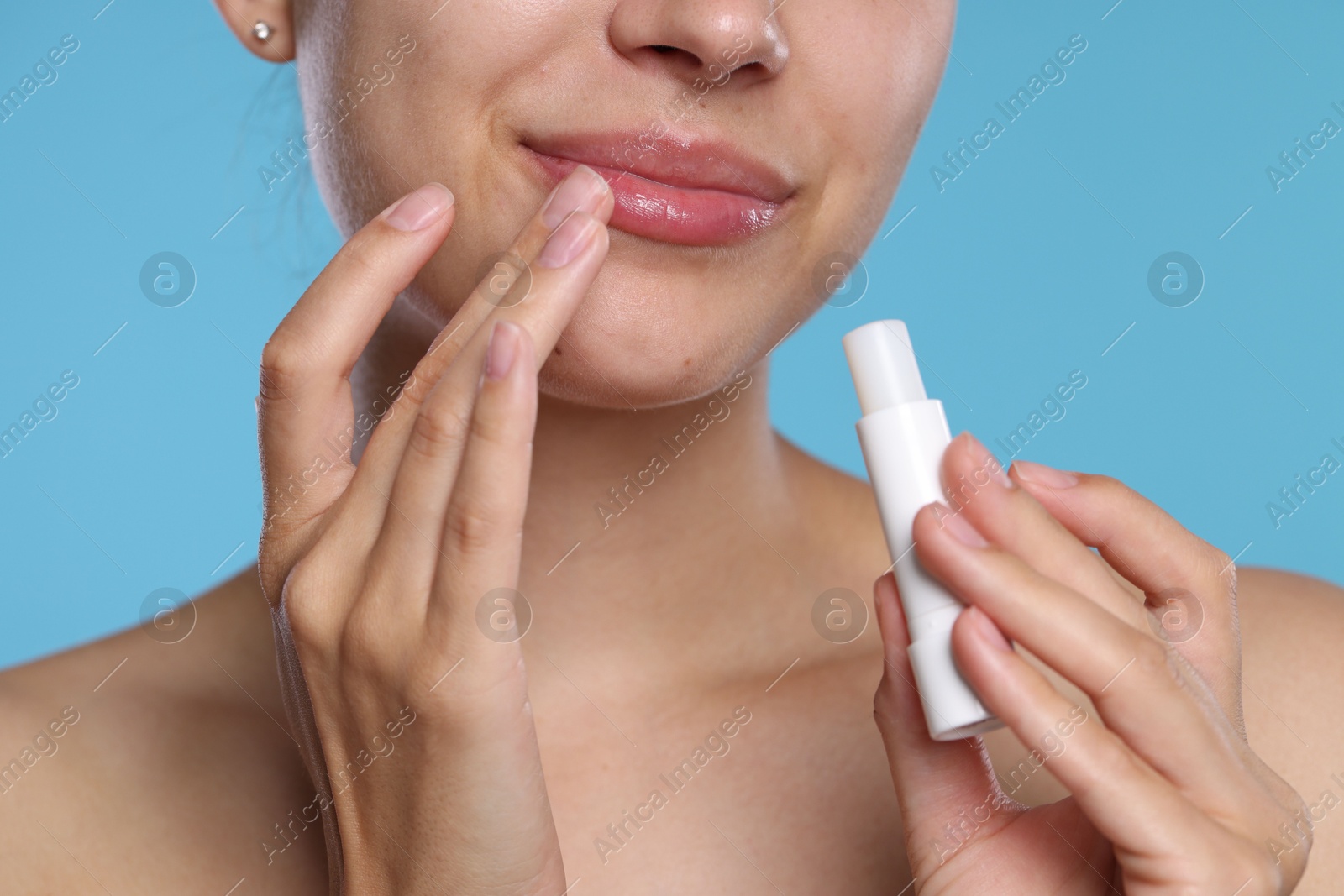 Young woman with lip balm on light blue background, closeup Photo of Young woman with lip balm on light blue background, closeup