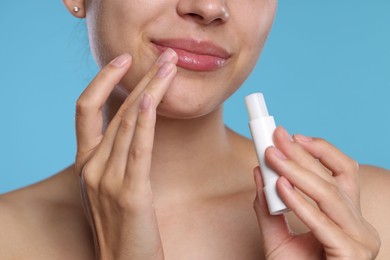 Photo of Young woman with lip balm on light blue background, closeup