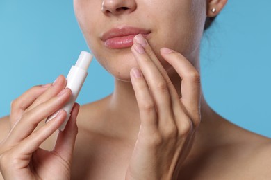 Photo of Young woman with lip balm on light blue background, closeup
