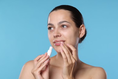 Photo of Young woman with lip balm on light blue background