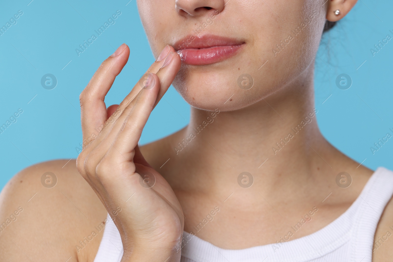 Young woman with lip balm on her lips against light blue background, closeup Photo of Young woman with lip balm on her lips against light blue background, closeup