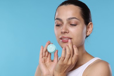 Photo of Young woman with lip balm on light blue background, space for text