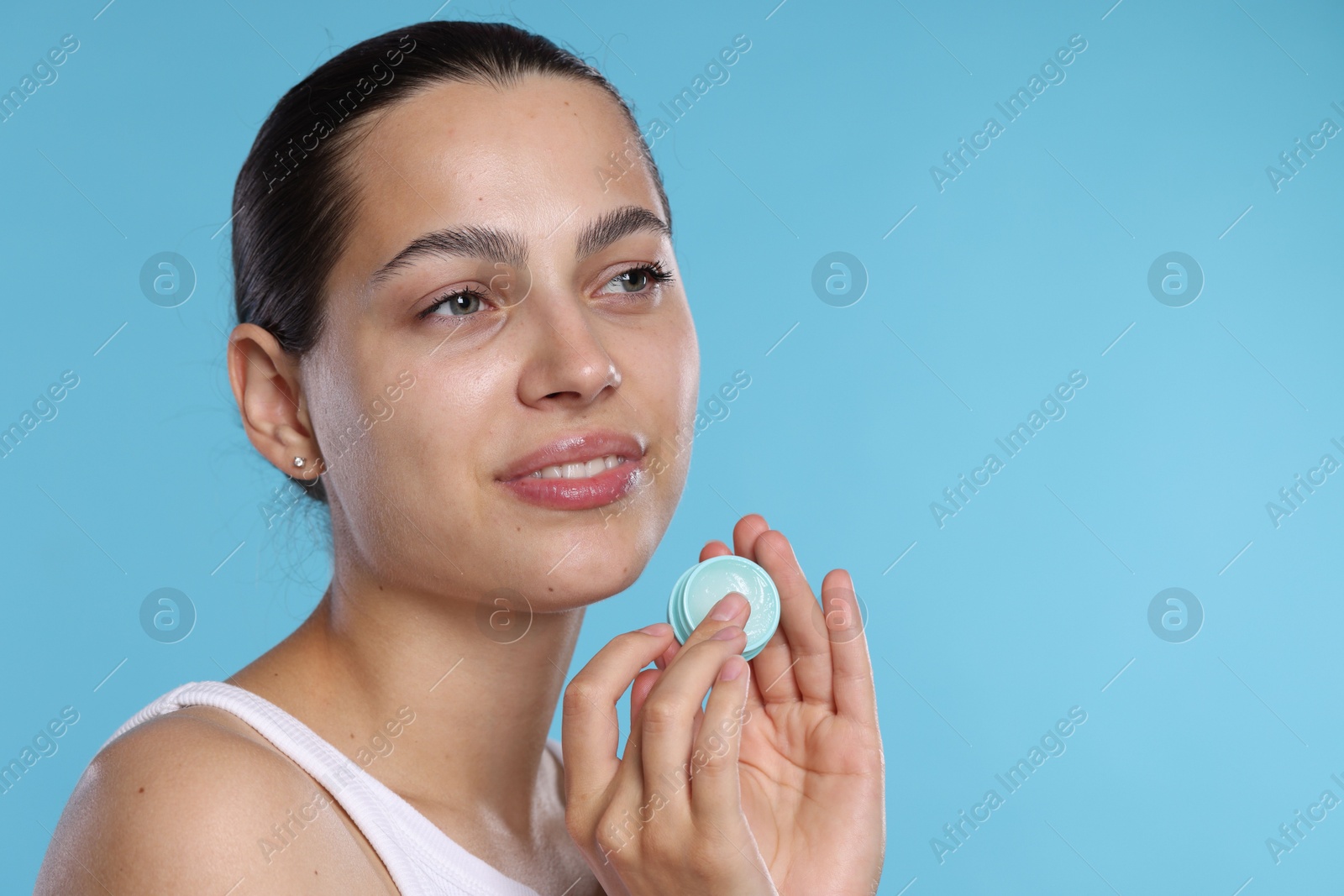 Photo of Young woman with lip balm on light blue background, space for text