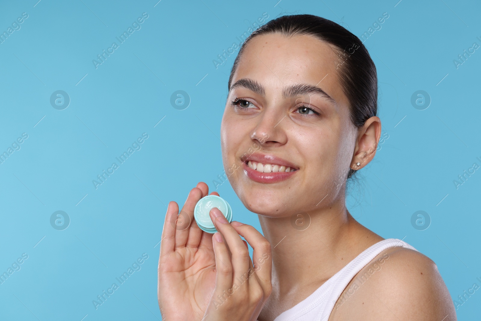 Young woman with lip balm on light blue background, space for text Photo of Young woman with lip balm on light blue background, space for text