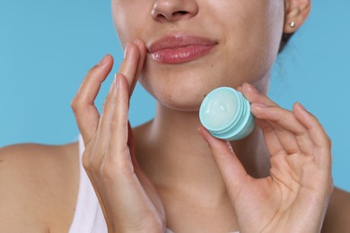 Photo of Young woman with lip balm on light blue background, closeup