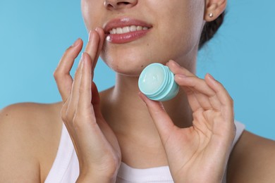 Photo of Young woman with lip balm on light blue background, closeup