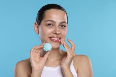 Photo of Young woman with lip balm on light blue background