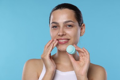Photo of Young woman with lip balm on light blue background