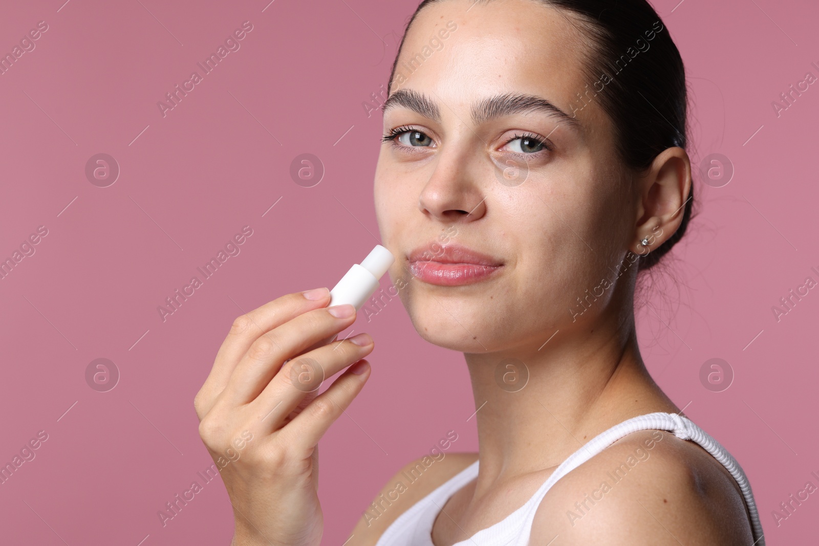 Young woman with lip balm on pink background Photo of Young woman with lip balm on pink background