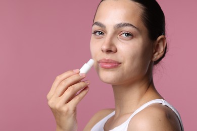 Photo of Young woman with lip balm on pink background