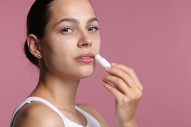 Photo of Young woman with lip balm on pink background