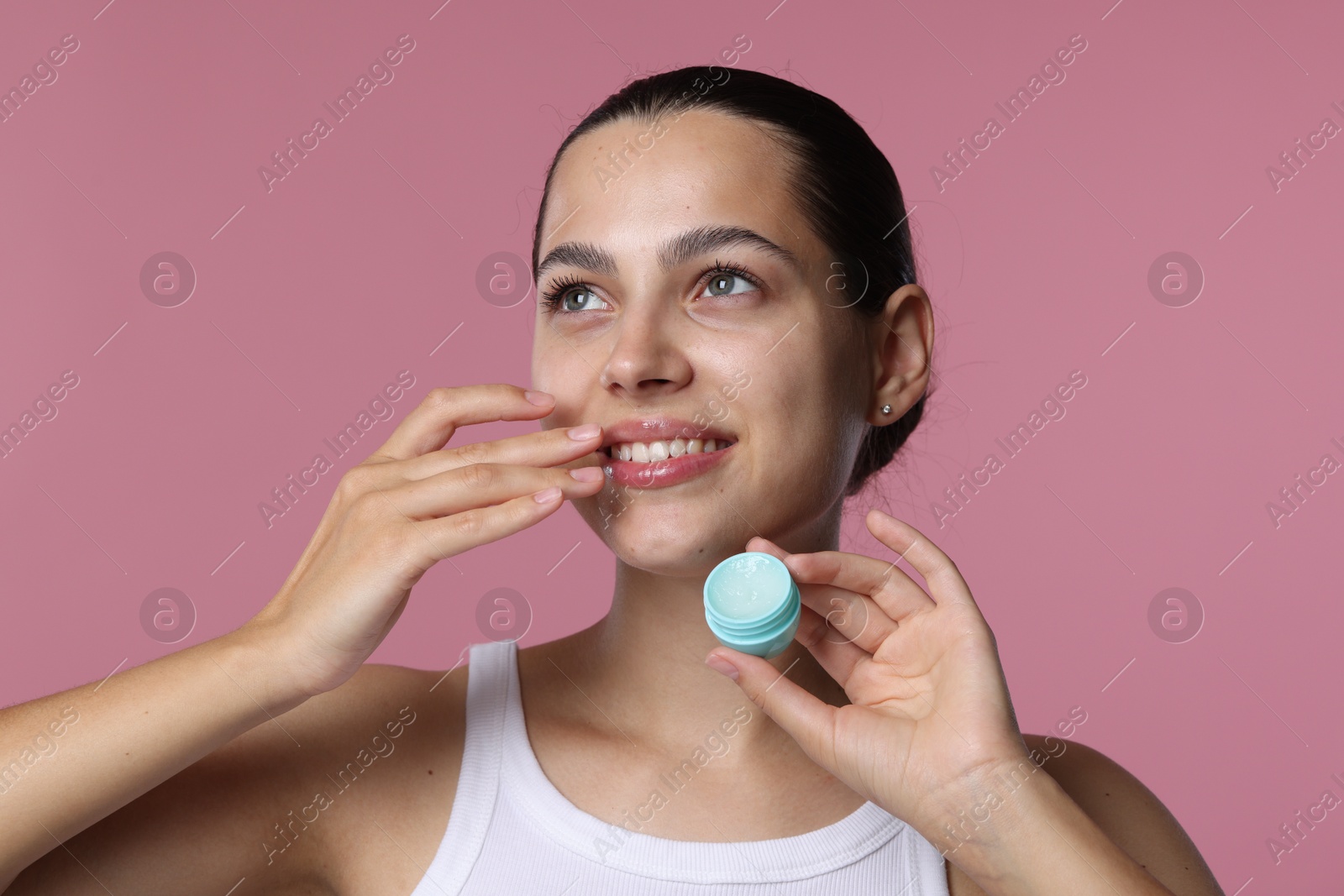 Young woman with lip balm on pink background Photo of Young woman with lip balm on pink background