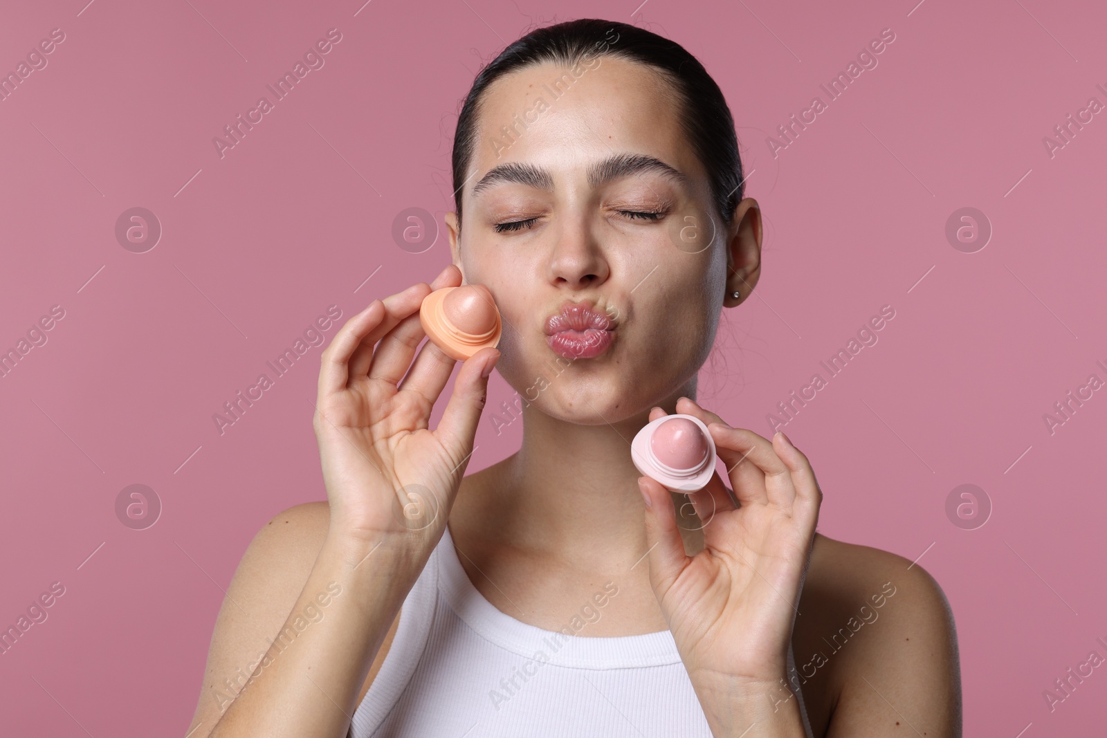 Young woman with lip balms on pink background Photo of Young woman with lip balms on pink background
