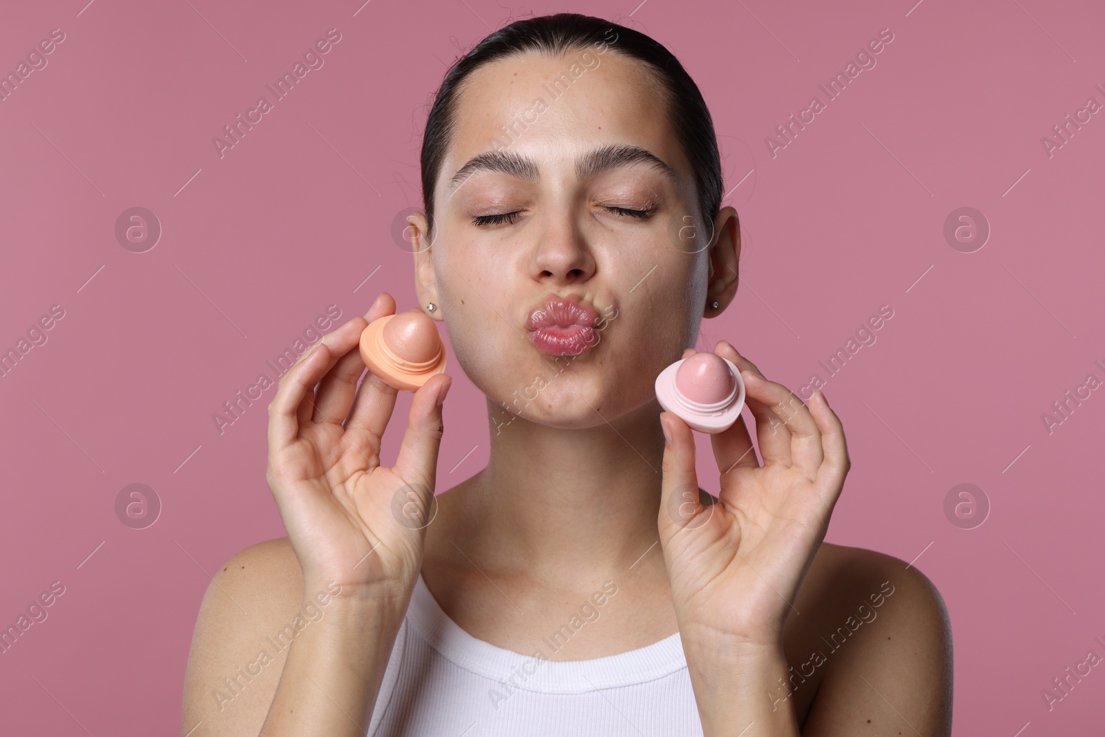 Young woman with lip balms on pink background Photo of Young woman with lip balms on pink background