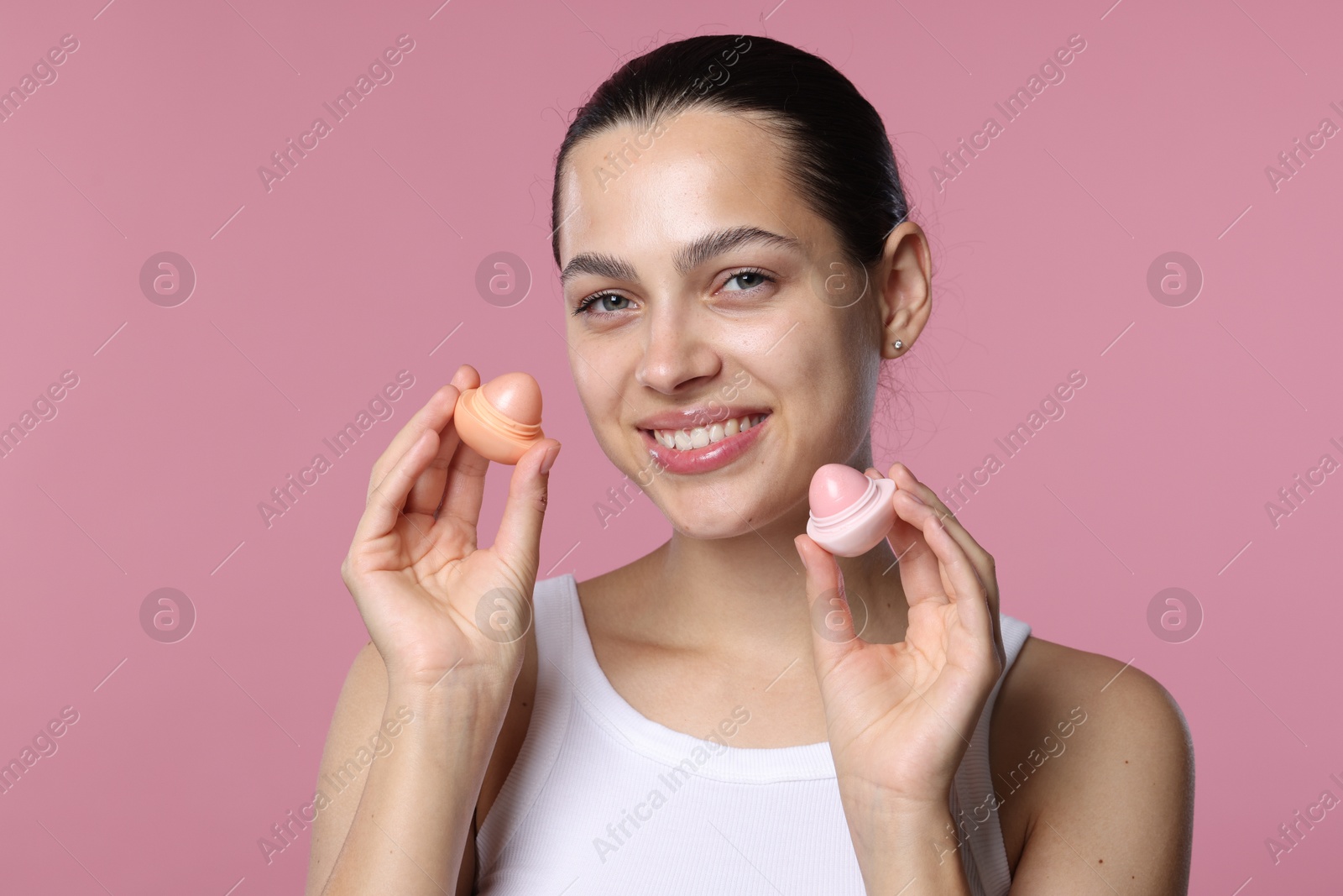 Young woman with lip balms on pink background Photo of Young woman with lip balms on pink background