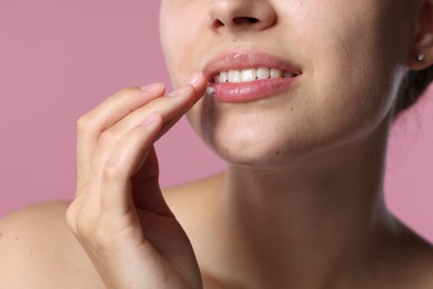 Photo of Young woman with lip balm on her lips against pink background, closeup