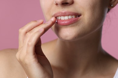 Photo of Young woman with lip balm on her lips against pink background, closeup