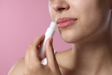 Photo of Young woman with lip balm on pink background, closeup