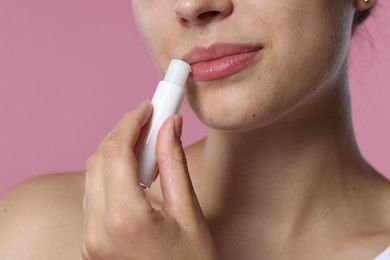 Photo of Young woman with lip balm on pink background, closeup