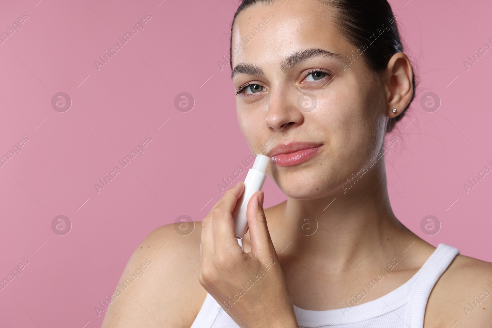 Photo of Young woman with lip balm on pink background, space for text