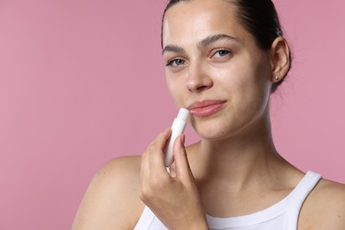 Photo of Young woman with lip balm on pink background, space for text