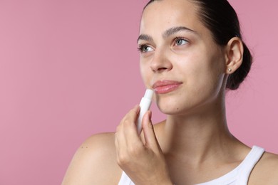 Photo of Young woman with lip balm on pink background, space for text