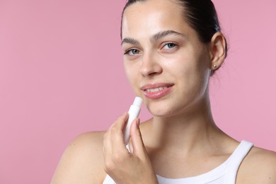 Photo of Young woman with lip balm on pink background, space for text