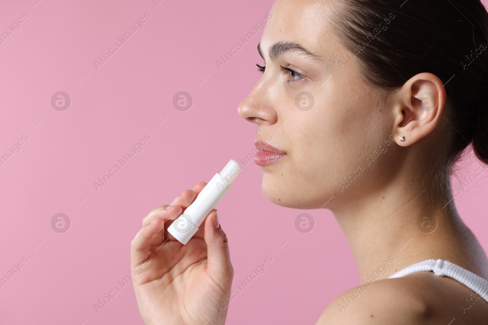 Young woman with lip balm on pink background, space for text Photo of Young woman with lip balm on pink background, space for text