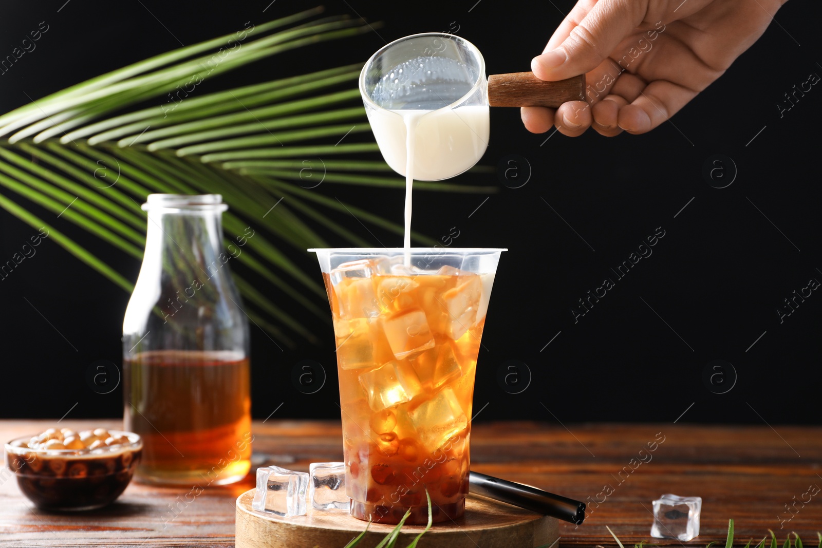 Woman pouring milk into bubble tea at wooden table, closeup Photo of Woman pouring milk into bubble tea at wooden table, closeup