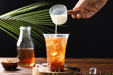 Photo of Woman pouring milk into bubble tea at wooden table, closeup