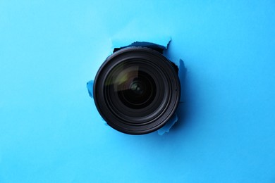 Photo of Hidden camera lens through torn hole in light blue paper