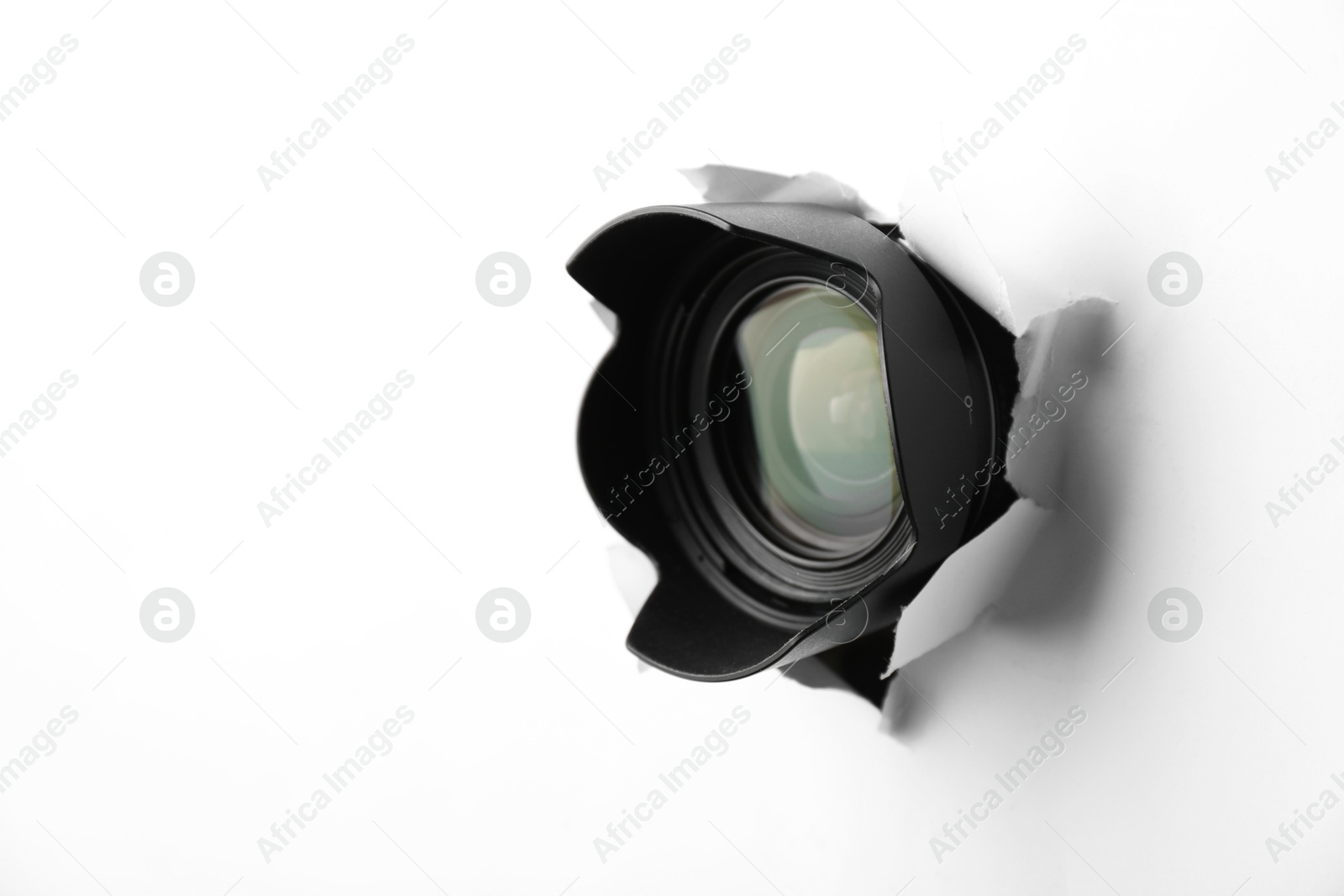 Photo of Hidden camera lens through torn hole in white paper. Space for text
