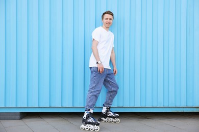 Photo of Happy young man with roller skates near light blue wall outdoors
