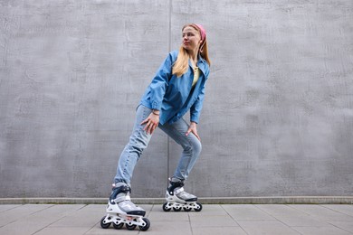 Photo of Beautiful young woman with roller skates near gray wall outdoors, low angle view