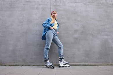 Photo of Beautiful young woman with roller skates near gray wall outdoors, low angle view