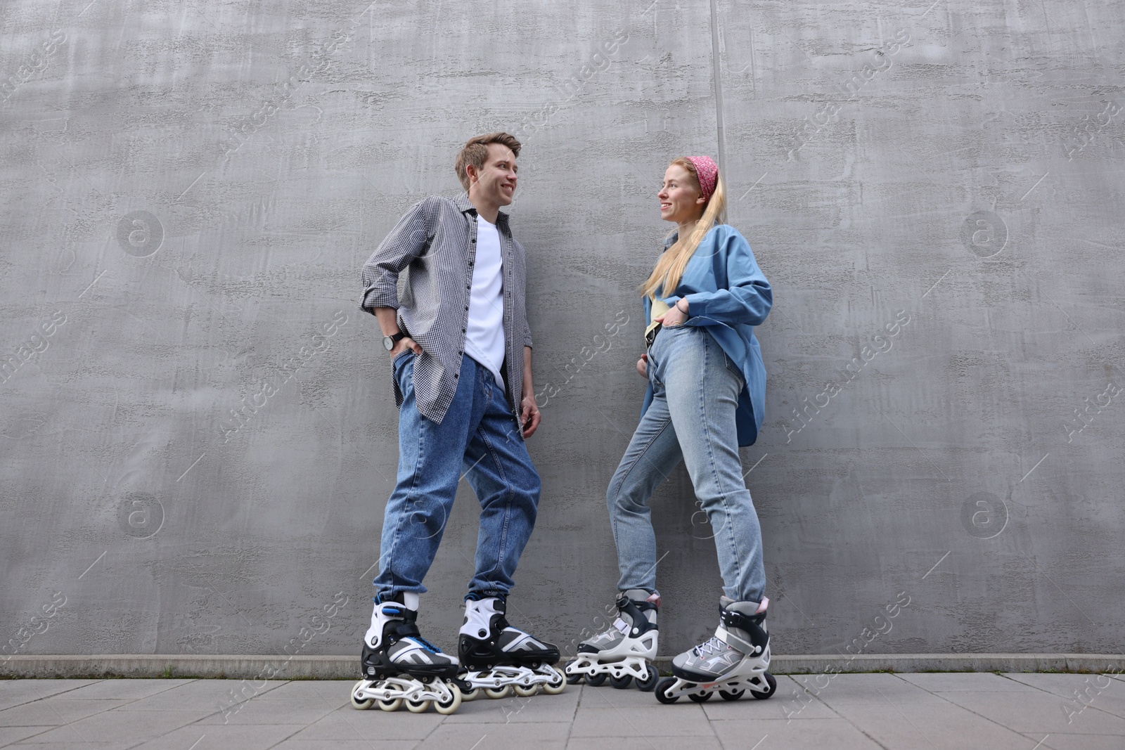Happy couple with roller skates near gray wall outdoors, low angle view Photo of Happy couple with roller skates near gray wall outdoors, low angle view