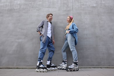 Photo of Happy couple with roller skates near gray wall outdoors, low angle view