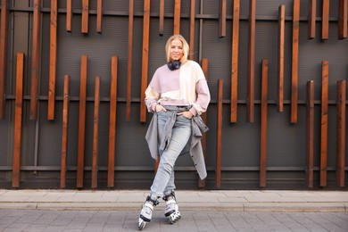 Photo of Beautiful young woman with roller skates near building outdoors