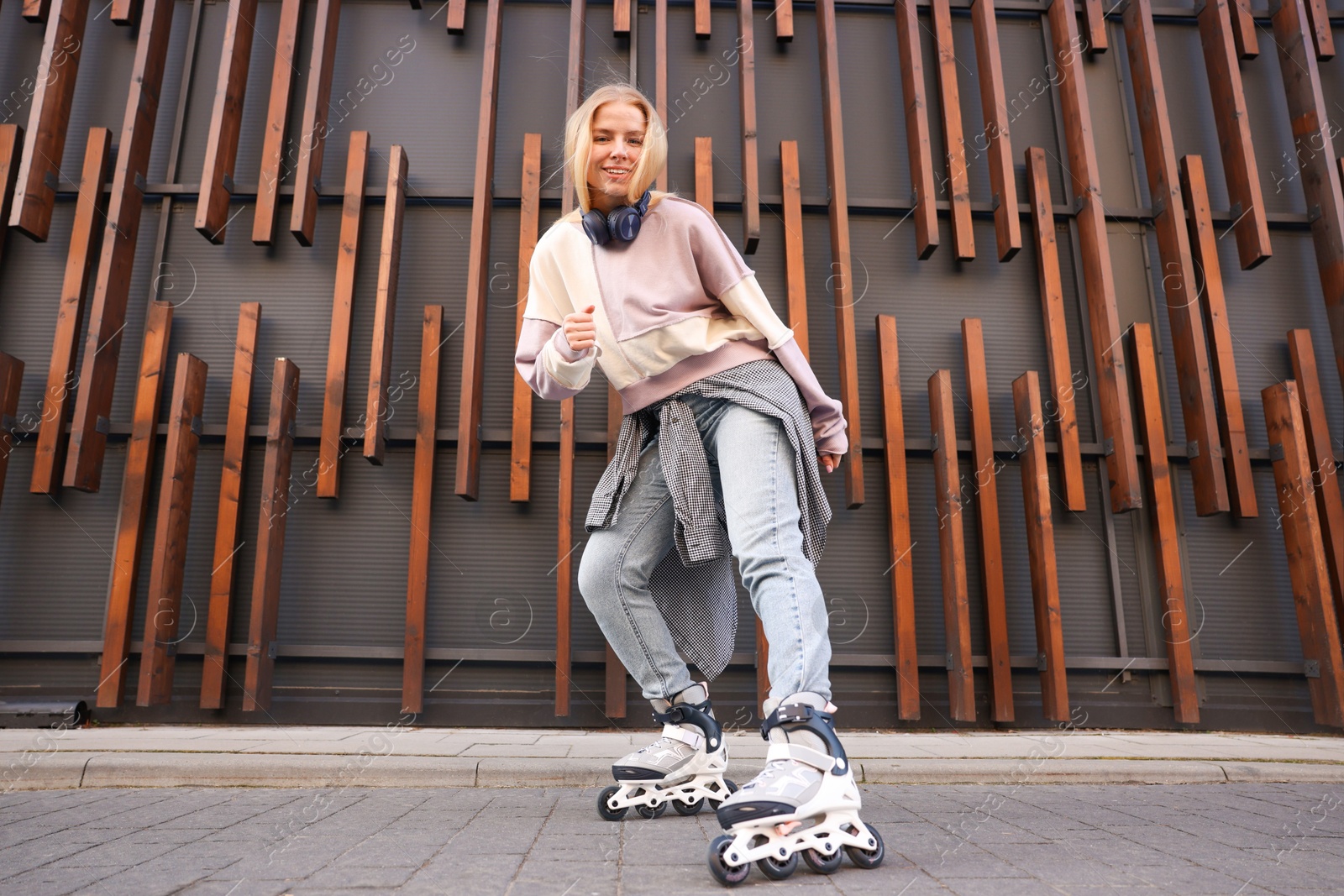 Beautiful young woman with roller skates near building outdoors, low angle view Photo of Beautiful young woman with roller skates near building outdoors, low angle view